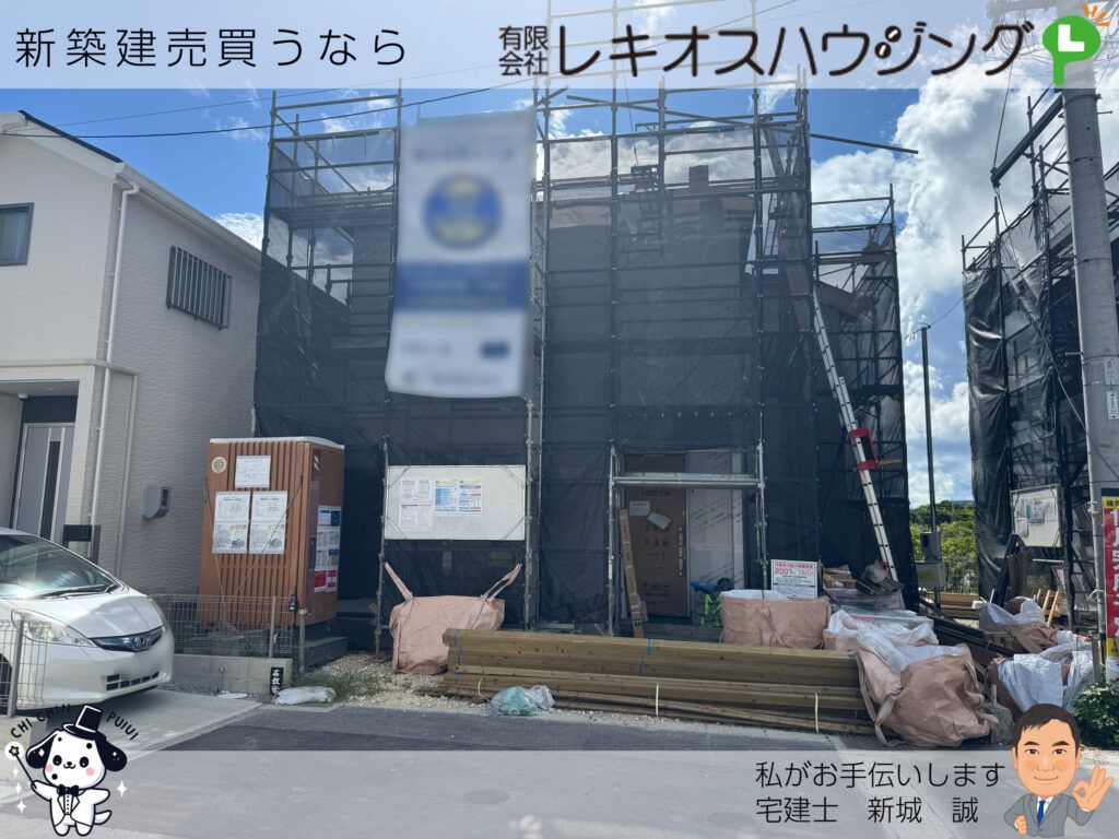 足場と養生シートに覆われた建築中の建物と積まれた資材