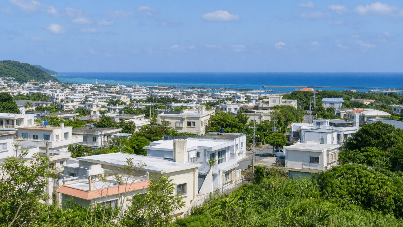 高台から見渡した沖縄の住宅街と青い海。白い陸屋根の住宅が並ぶ