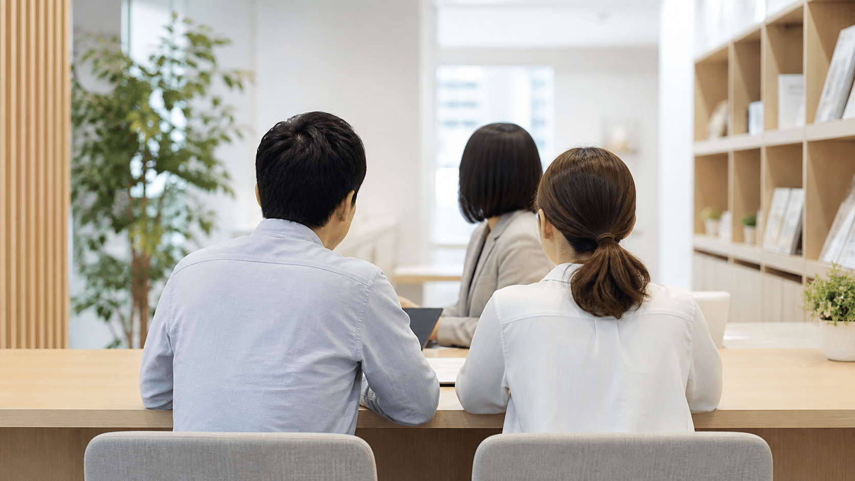不動産会社のカウンターで相談する夫婦。後ろ姿