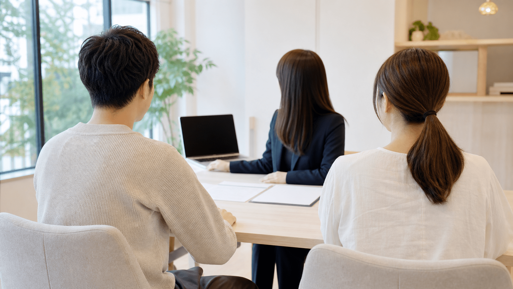 明るい相談スペースで担当者と向き合って話す夫婦。後ろ姿