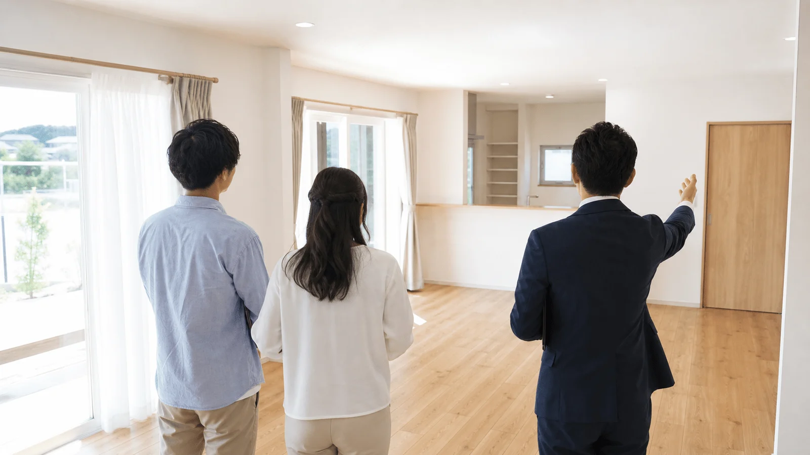 明るいリビングで購入希望の夫婦を案内する不動産会社の担当者。後ろ姿