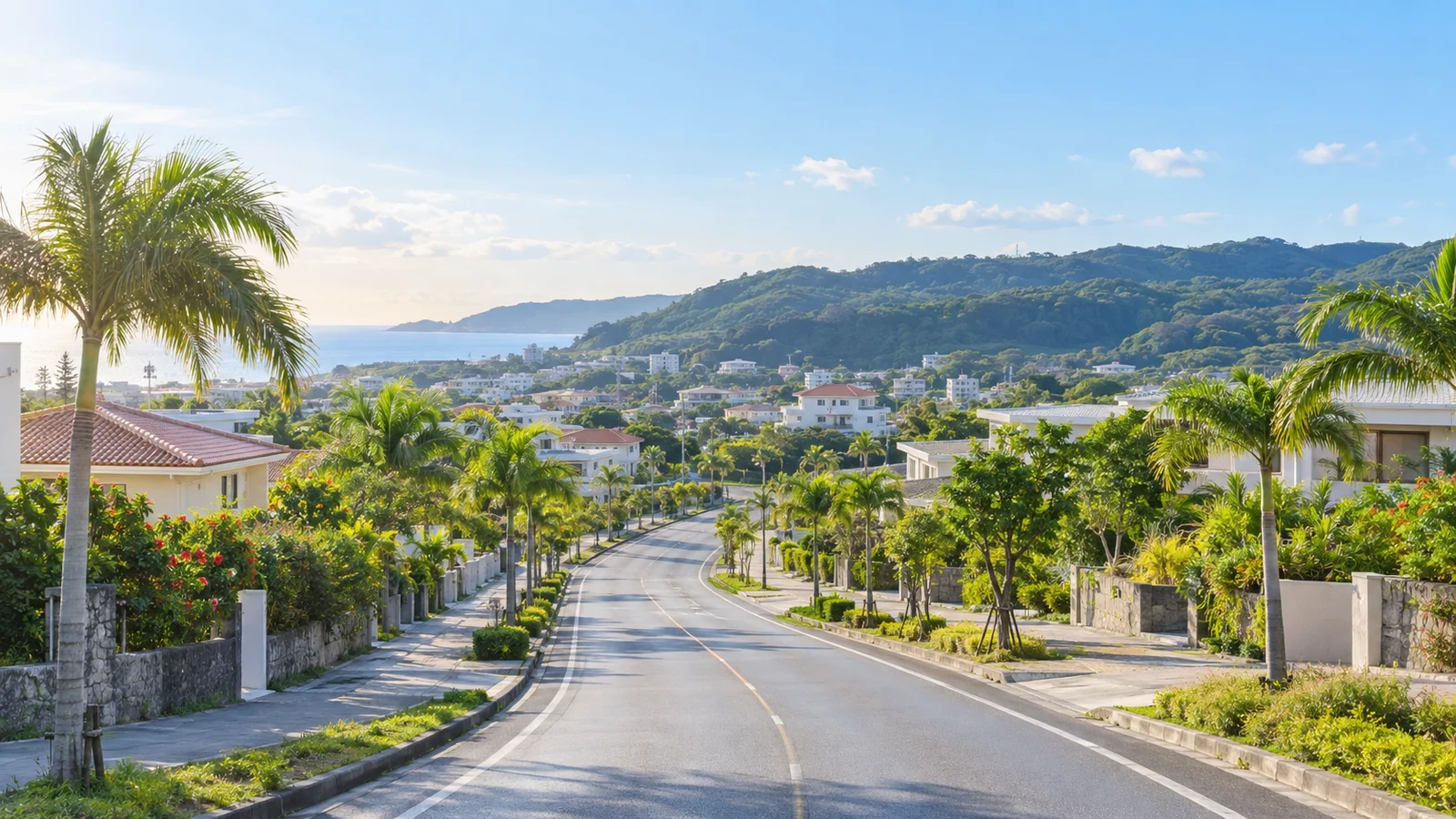 ヤシの木が並ぶ、住宅街を抜ける郊外の道路。遠くに海と山が見える