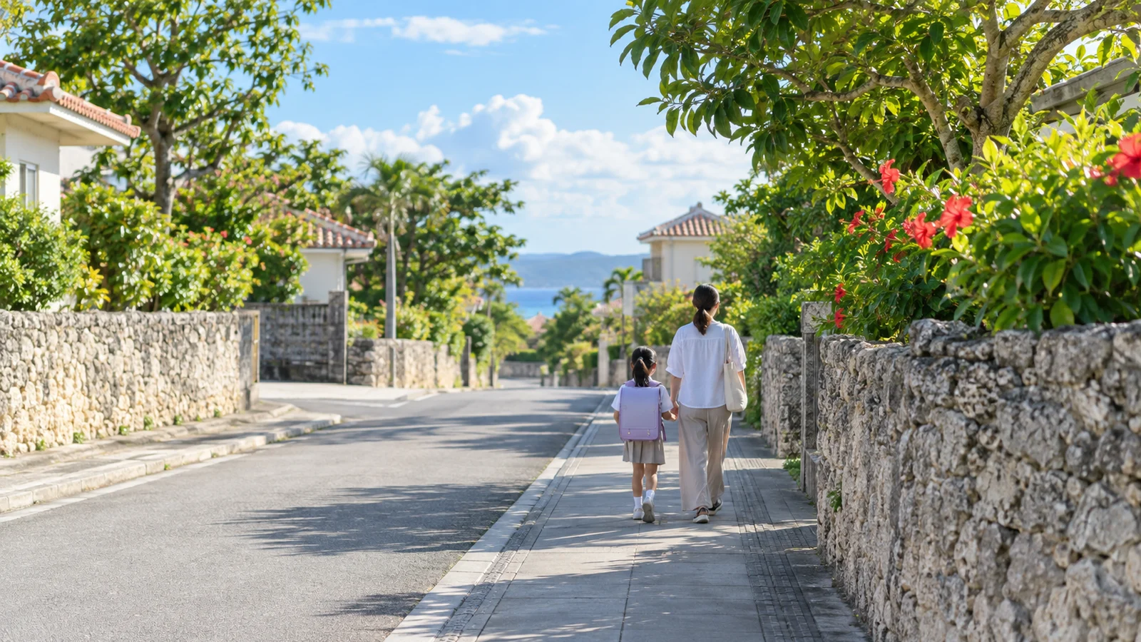 石垣の続く住宅街の歩道を歩く、ランドセルの子どもと大人の後ろ姿