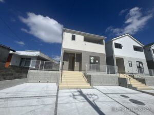 白とグレーの外壁の2階建て。前面にコンクリート敷きの駐車スペースと玄関への階段がある外観です