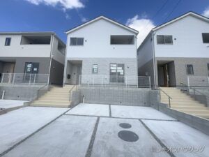 白とグレーの外壁の2階建て。両隣にも新築の住宅が並ぶ外観です