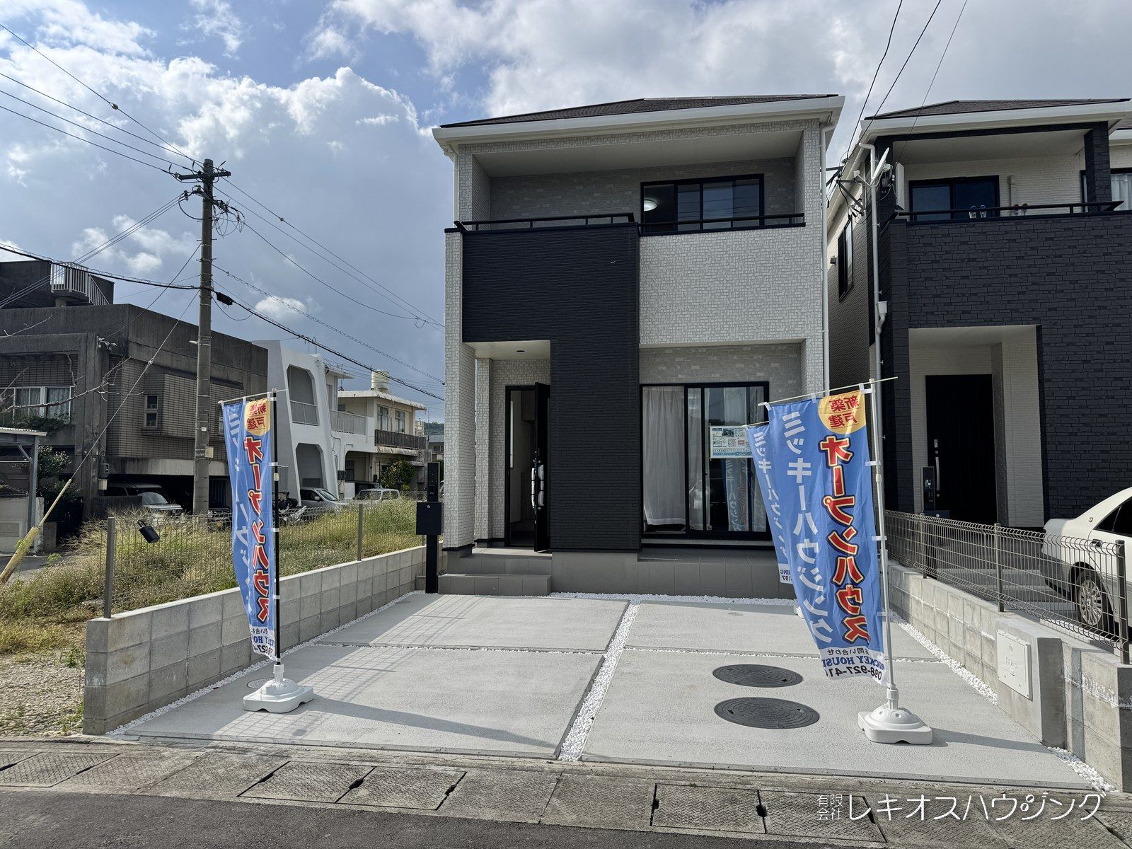 白と黒の外壁の2階建て。建物の前面にコンクリート敷きの駐車スペースがある外観です